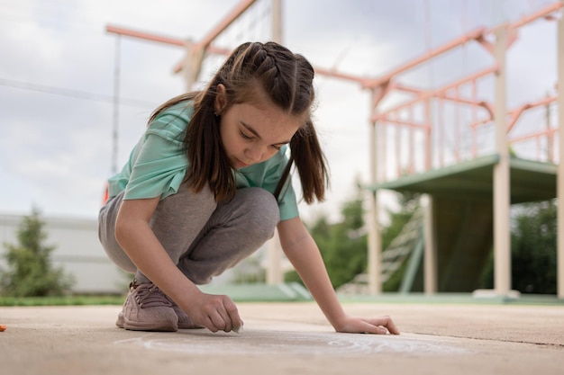 La ragazza disegna con i pastelli colorati sul marciapiede disegni dei bambini con il gesso sul muro bambino creativo gioia dell'infanzia