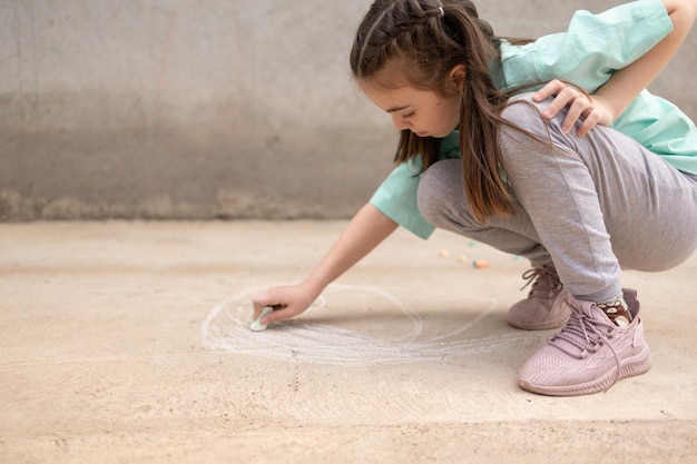 Girl draws with colorful crayons on pavement Children39s drawings with chalk on wall Creative kid Joy of childhood