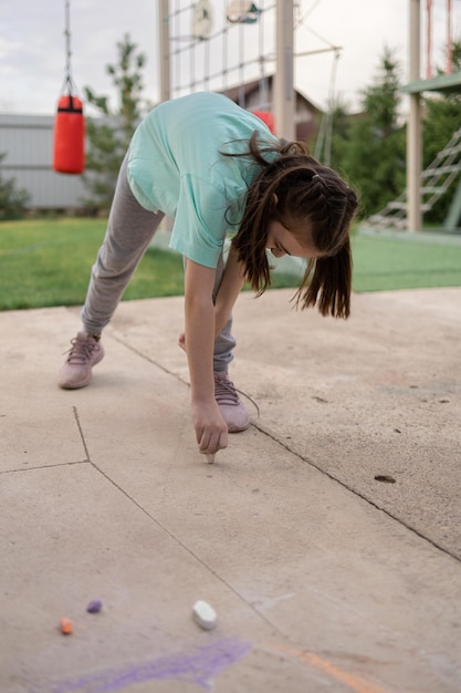 Girl draws with colorful crayons on pavement