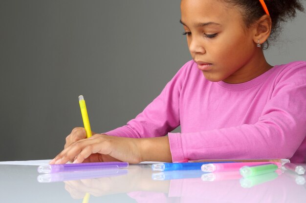 The girl draws a yellow pencil on white paper