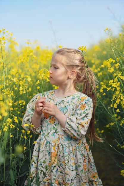 A girl in a dress in a field of rapeseed smelling flowers