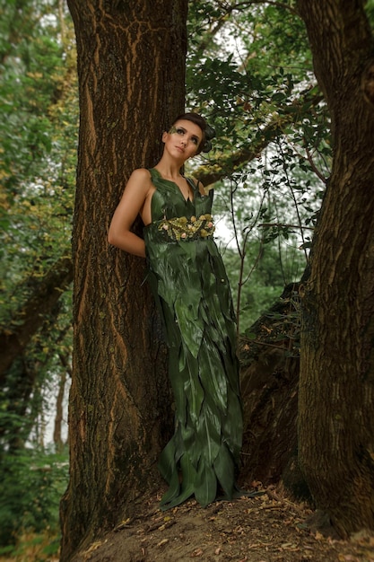 Girl in a dress of green palm leaves on a forest lake