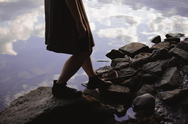 Girl in a dress and sneakers walking on the rocks on the lake