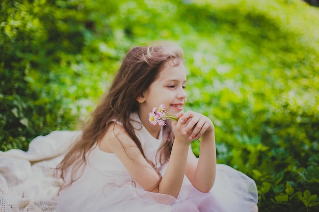 A girl in dress sniffs a bouquet of daisies in spring cherry garden