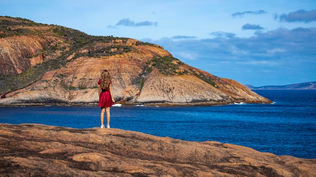 Foto ragazza in abito si erge sulle rocce in riva all'oceano nell'australia occidentale bellissimo paradiso baie esperance
