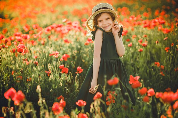 Girl in dress and straw hat outdoor At Poppy Field on sunset