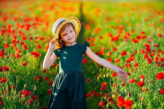 Ragazza in vestito e cappello di paglia all'aperto al campo di papaveri