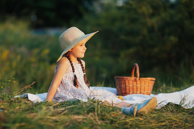 girl in dress and straw hat sitting on the green grass in the park