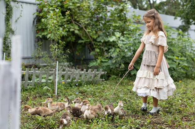 Girl in a dress with an apron grazes ducklings