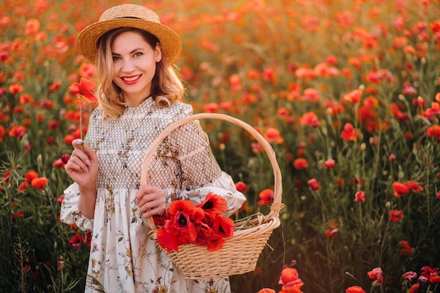 A girl in a dress with a hat and with a basket in a field with poppies