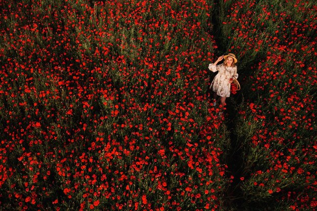 A girl in a dress with a hat and with a basket in a field with poppies