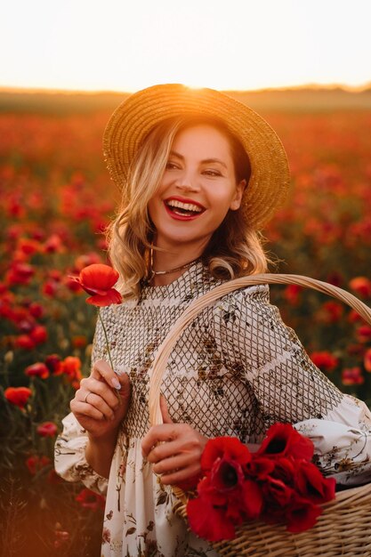 A girl in a dress with a hat and with a basket in a field with poppies