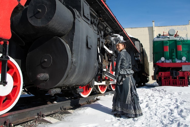 Girl dressed as a noblewoman of the 19th century near a steam locomotive Russian winter