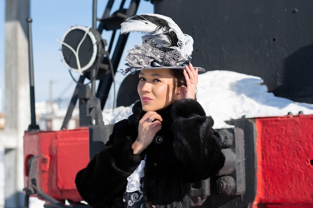 蒸気機関車の近くで19世紀の貴婦人に扮した少女。ロシアの冬