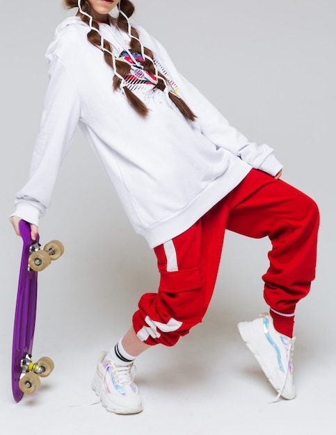 A girl dressed in casual clothes in a sports style holds a\
purple skateboard in her hands. vertical photo