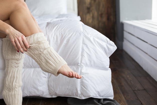 Girl dresses knee socks sitting on the bed in the bedroom.