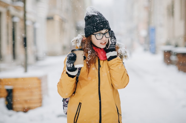Девушка пьет кофе и разговаривает по телефону на улице в зимний период