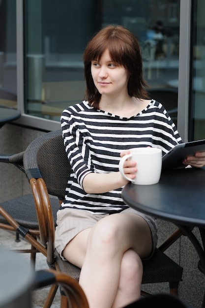 Girl drinking coffee and using tablet computer in a outdoor cafe