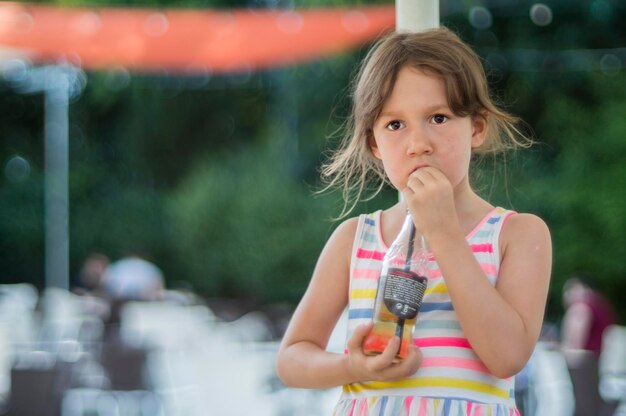 Photo girl drinking cold drink from bottle while standing at outdoor cafe