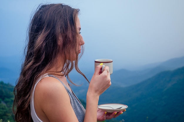 Girl drinking cup of hot tea on top mountain in india herb
plantation