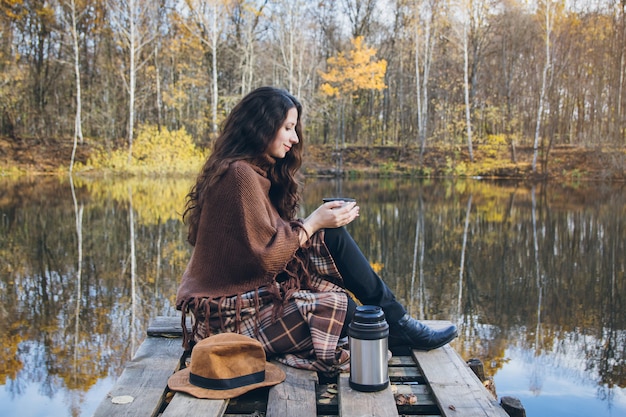 湖の木製の橋でお茶を飲む女の子