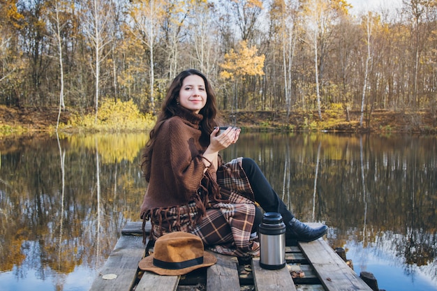 Девушка пьет чай на деревянный мост на озере