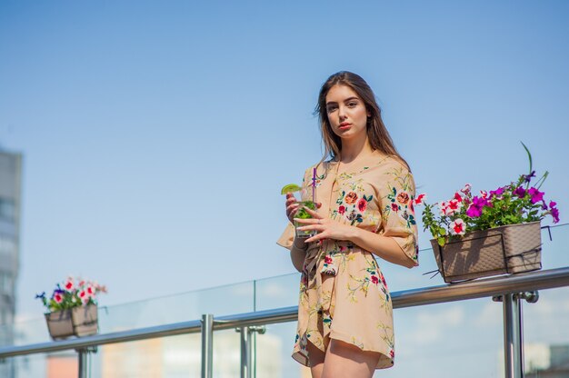 Girl drinks cold mojito with ice on a hot, sultry summer day against the background of the city.