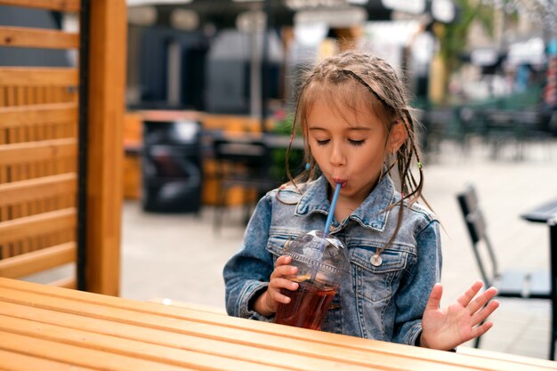 A girl drinks lemonade from a straw while sitting at a table a city cafe