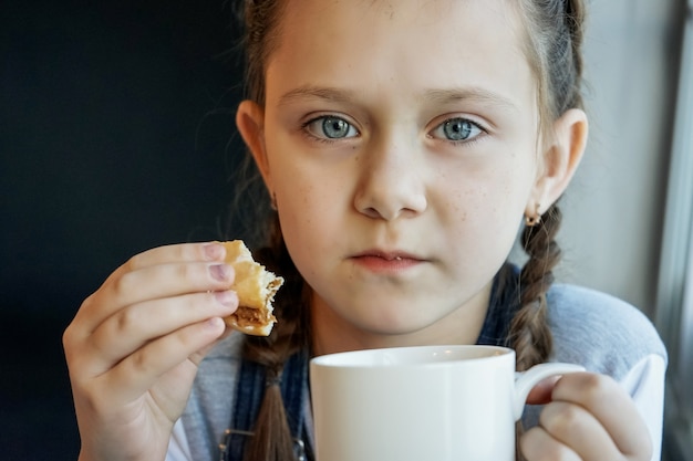Девушка пьет чай и ест печенье во время самоизоляции. коронавирус covid-19. остаться дома