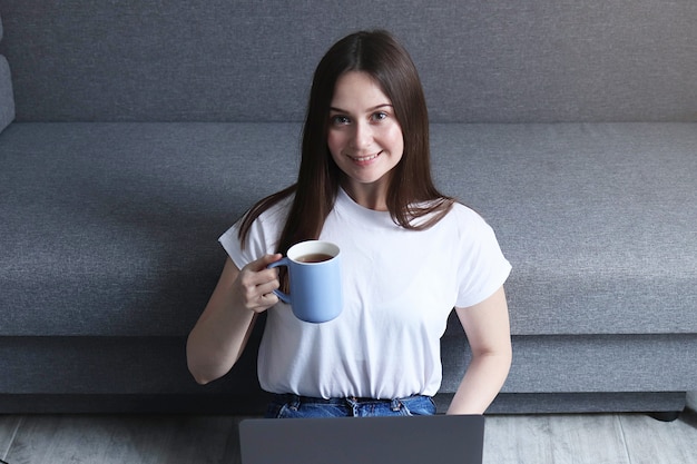 Girl drinks tea and works on laptop