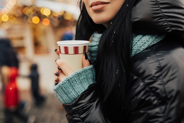 女の子はクリスマスマーケットで温かい飲み物を飲みます