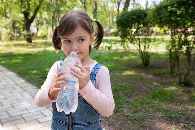 The girl drinks water from a bottle in the park