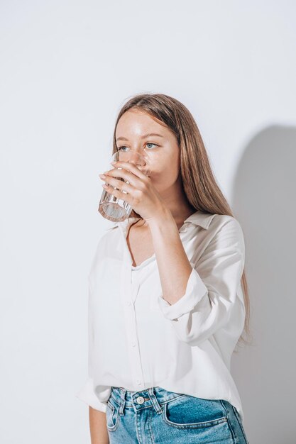 白い背景のガラスのカップから水を飲む少女 水のバランスを維持する概念