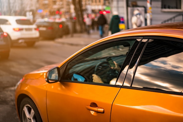 Girl driving orange car with smart phone in hand. City drive road