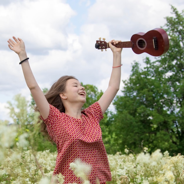 Photo the girl in the early morning walks on the meadow with ukulele