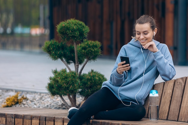 Девушка в наушниках держит смартфон, отправляя текстовые сообщения, прокручивая чтение