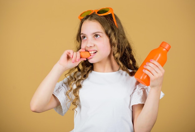 Девушка ест морковные овощи и пьет морковный сок летние каникулы маленькая девочка в модных очках Витаминное питание освежающий витаминный сок Здравоохранение Здоровая пища - это здоровая жизнь