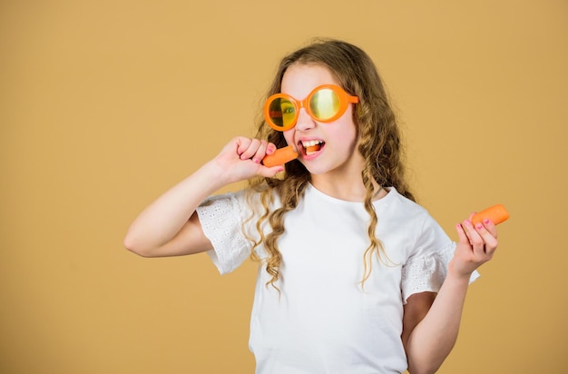 Girl eat carrot vegetable and drink carrot juice Vitamin nutrition Fashion kid sunglasses drink refreshing vitamin juice Health care Summer vitamin diet Happy childhood Natural vitamin source