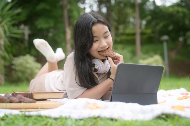 公園でパンを食べてコンピュータータブレットを使用している女の子