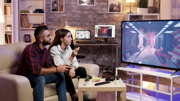 남자 친구가 텔레비전에서 비디오 게임을 하는 동안 칩을 먹는 소녀.