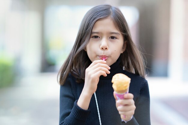 屋外でスプーンを使用してコーン型アイスクリームを食べる女の子