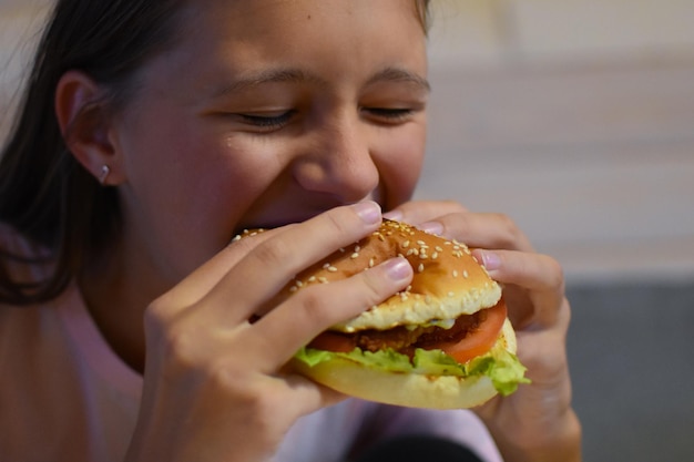 Ragazza che mangia hamburger delizioso degli alimenti a rapida preparazione con le patatine fritte.