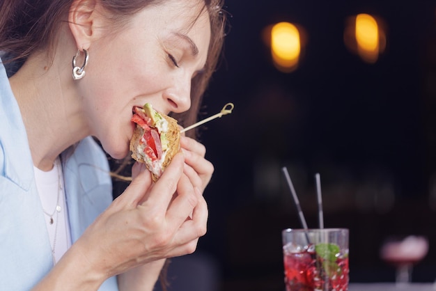 Girl eating delicious sandwich close up in modern cafe