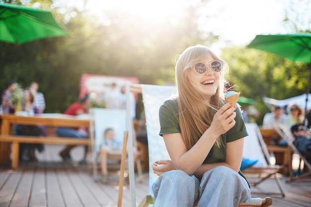 Ragazza che mangia il gelato ridendo ritratto di giovane donna seduta in un parco in una giornata di sole a mangiare il gelato guardando fuori dalla fotocamera con gli occhiali che si godono l'estate