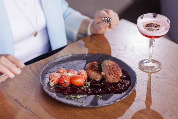 Girl eating meat medallion with tomatoes closeup in a modern restaurant