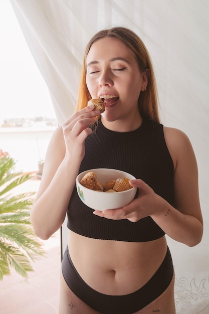 Girl eating muffins in front of a window