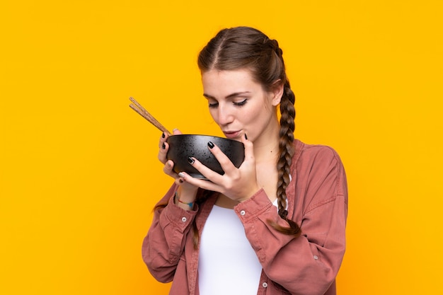 Girl eating noodles over isolated yellow wall