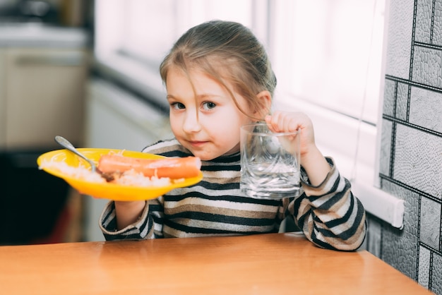 girl eating pasta with sausage in the kitchen in a striped jacket