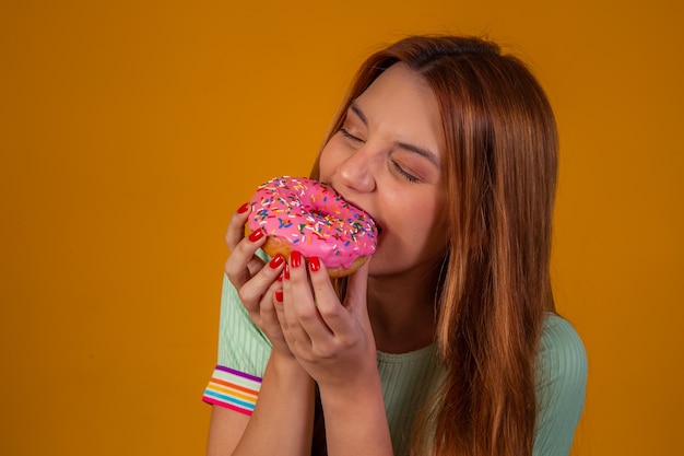 Girl eating pink donuts on yellow background.