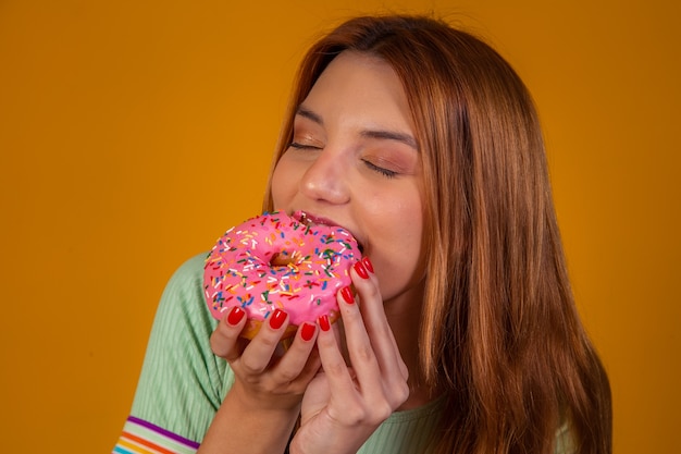 Girl eating pink donuts on yellow background.